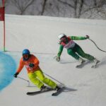 Vision Impaired Skier going down hill, with their sited guide in front of them.