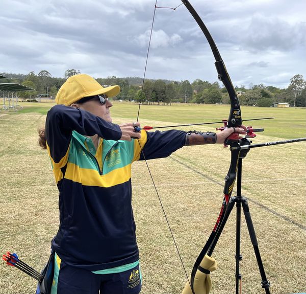 Image of Janelle Colquhoun drawing back her bow, ready to shoot arrow at target in preparation for Archery competiton. She is wearing her BSA games uniform.