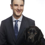 Image of Michael Sheppard smiling at camera, with his guide dog Larry sitting next to him