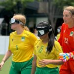 two Australian women's blind football team players and the goal keeper standing on field during a match