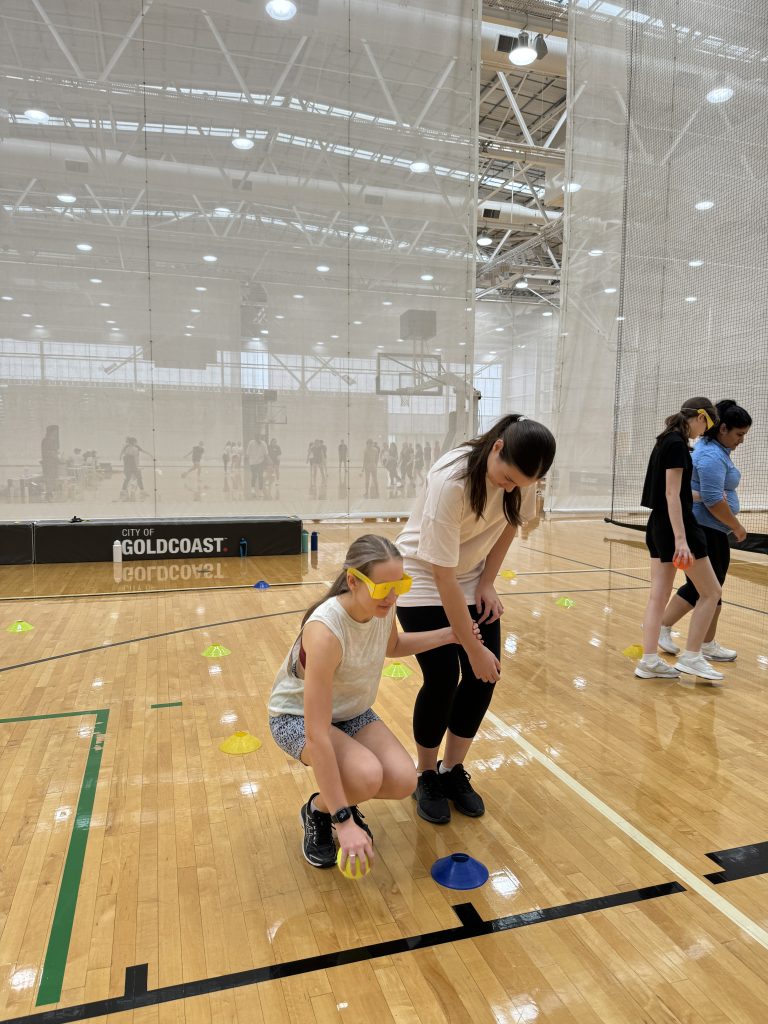 two teaching students utilising vision simulation glasses, learning to guide each other during a university inclusion sports day