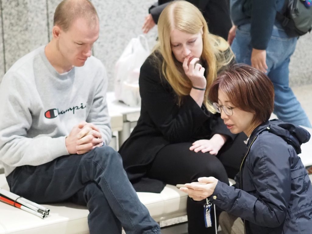 Brendan and Rachel experience a presentation and demonstration by Ashirase, Inc. regarding their navigation device for the visually impaired.